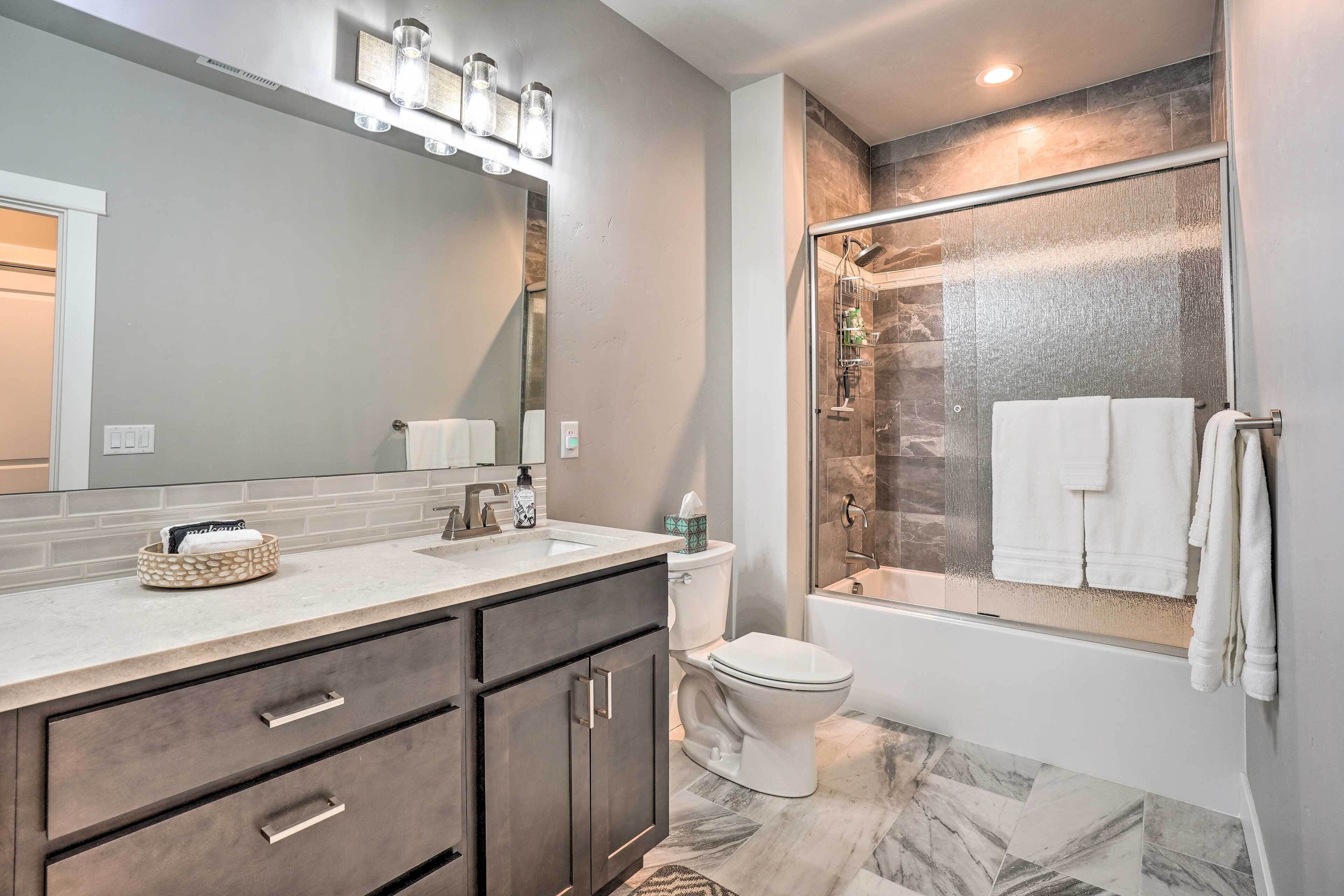 A modern bathroom with a large mirror, a vanity with drawers, a toilet, and a glass-enclosed shower.