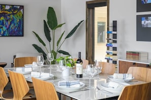 Uma mesa de jantar posta com pratos brancos, guardanapos e copos de vinho, uma garrafa de vinho e um vaso de plantas.