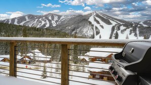Un paysage de montagne enneigé avec un balcon en bois et un barbecue.