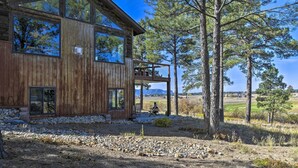 A rustic wooden cabin with large windows, a deck, and a view of a golf course. - Lake Pagosa Home w/ Hot Tub & Mtn/lake Views! (Pagosa Springs)