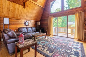 Ein Holzblockhaus-Innenraum mit einer Ledersofa, einem Couchtisch, einem Teppich und einem großen Fenster mit Vorhängen.