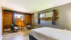 Ein Schlafzimmer mit einem Bett, zwei Stühlen, einem kleinen Tisch, einer Lampe und einem Fenster mit Vorhängen.