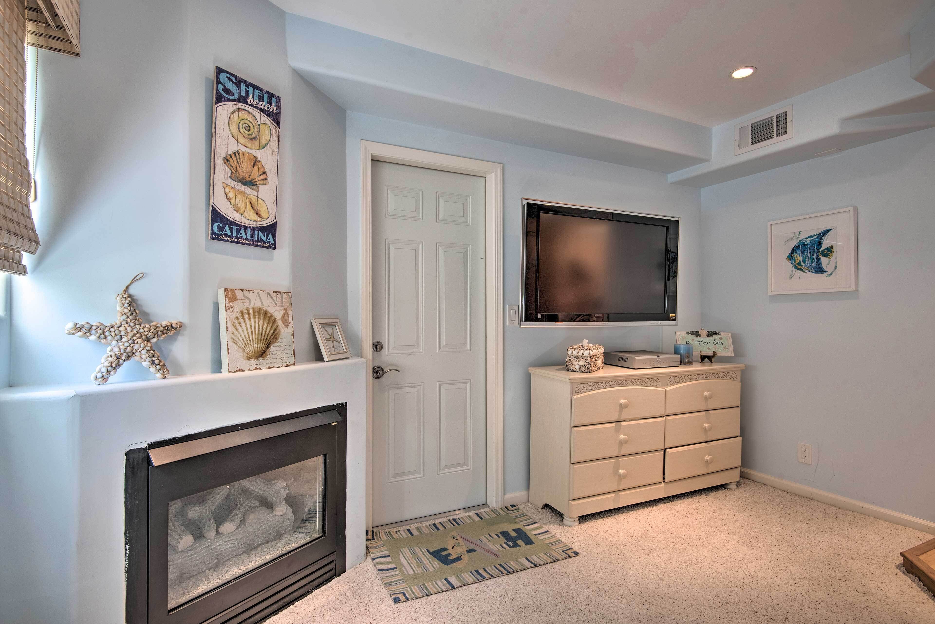 A room with a fireplace, a television mounted above a dresser, and decorative wall art.