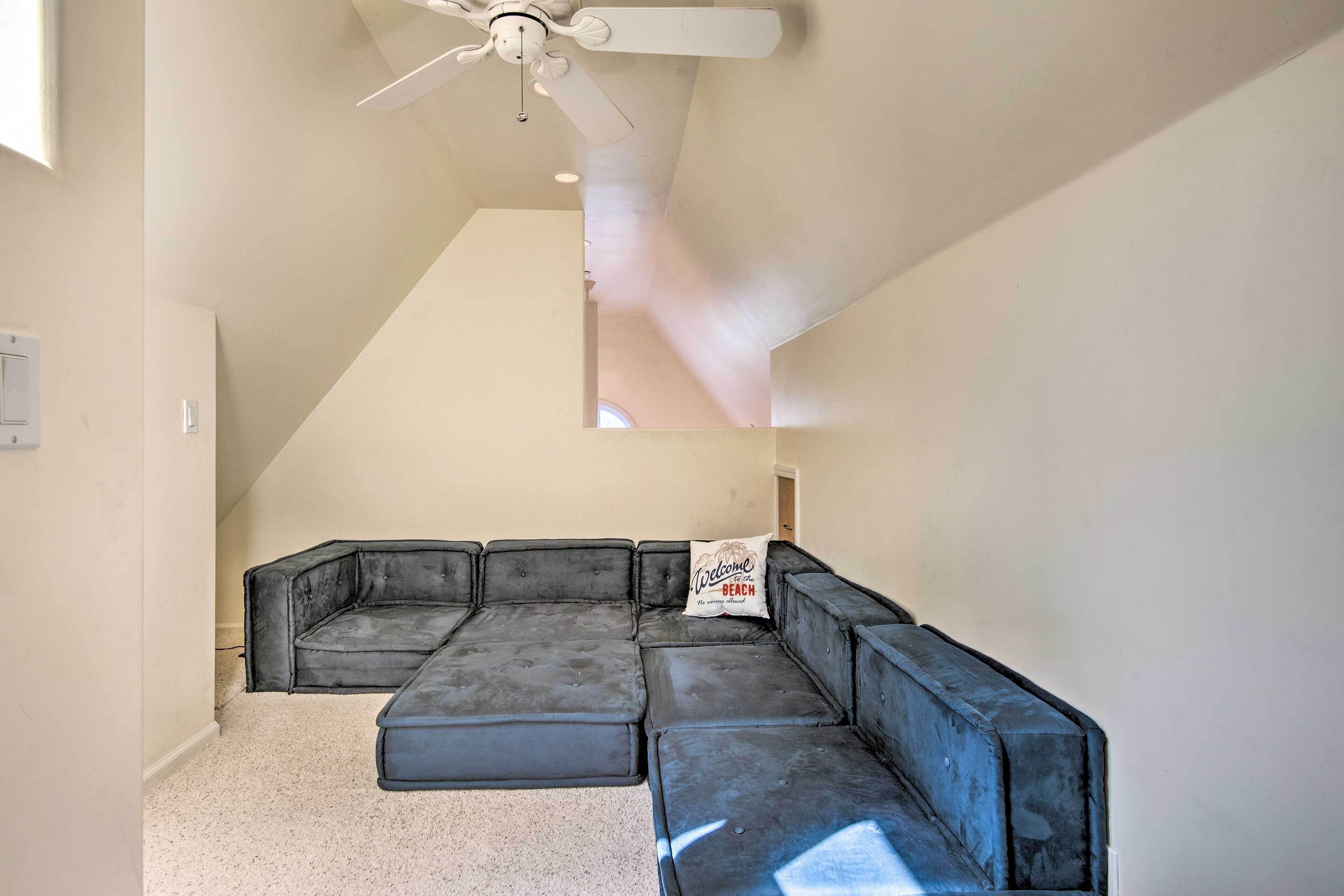 Una sala moderna con un sofá modular, un ventilador de techo y un techo inclinado.