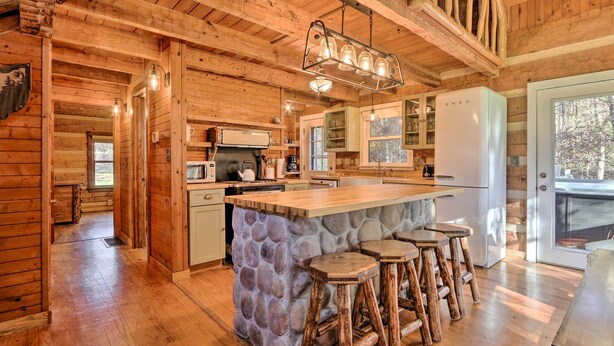 A rustic kitchen with wooden walls, a stone island, and bar stools. - Luxe Dog-friendly Cabin w/ Hot Tub & Game Room (Logan)