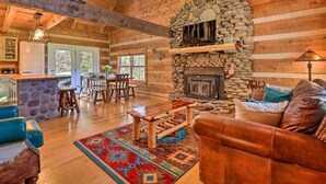 A rustic cabin interior with a stone fireplace, wooden furniture, and a stone wall. - Luxe Dog-friendly Cabin w/ Hot Tub & Game Room (Logan)