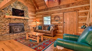 A log cabin interior with a stone fireplace, leather sofa, and a green leather chair. - Luxe Dog-friendly Cabin w/ Hot Tub & Game Room (Logan)