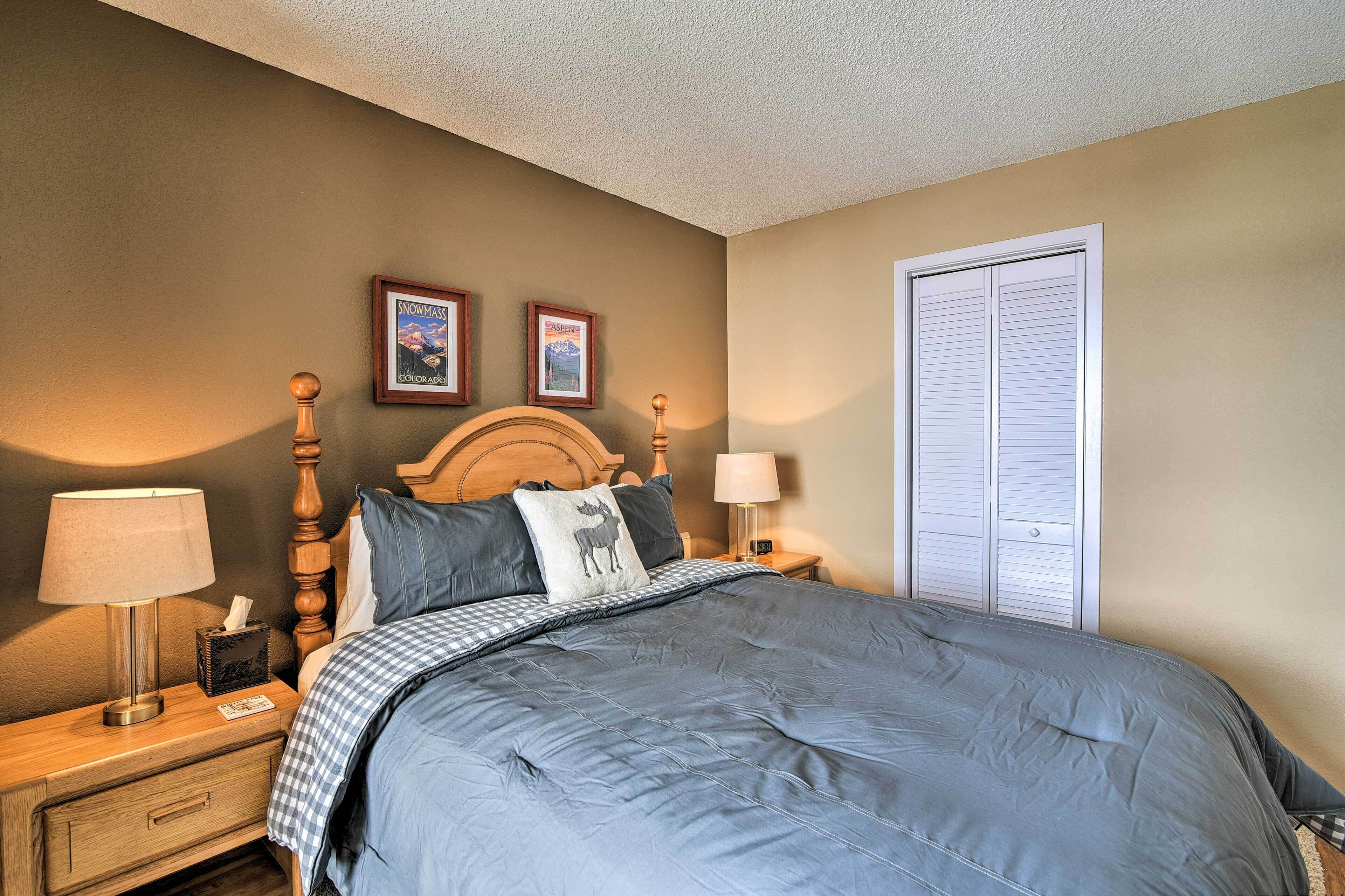 A bedroom with a bed, wooden headboard, two bedside tables with lamps, a nightstand, and a door.