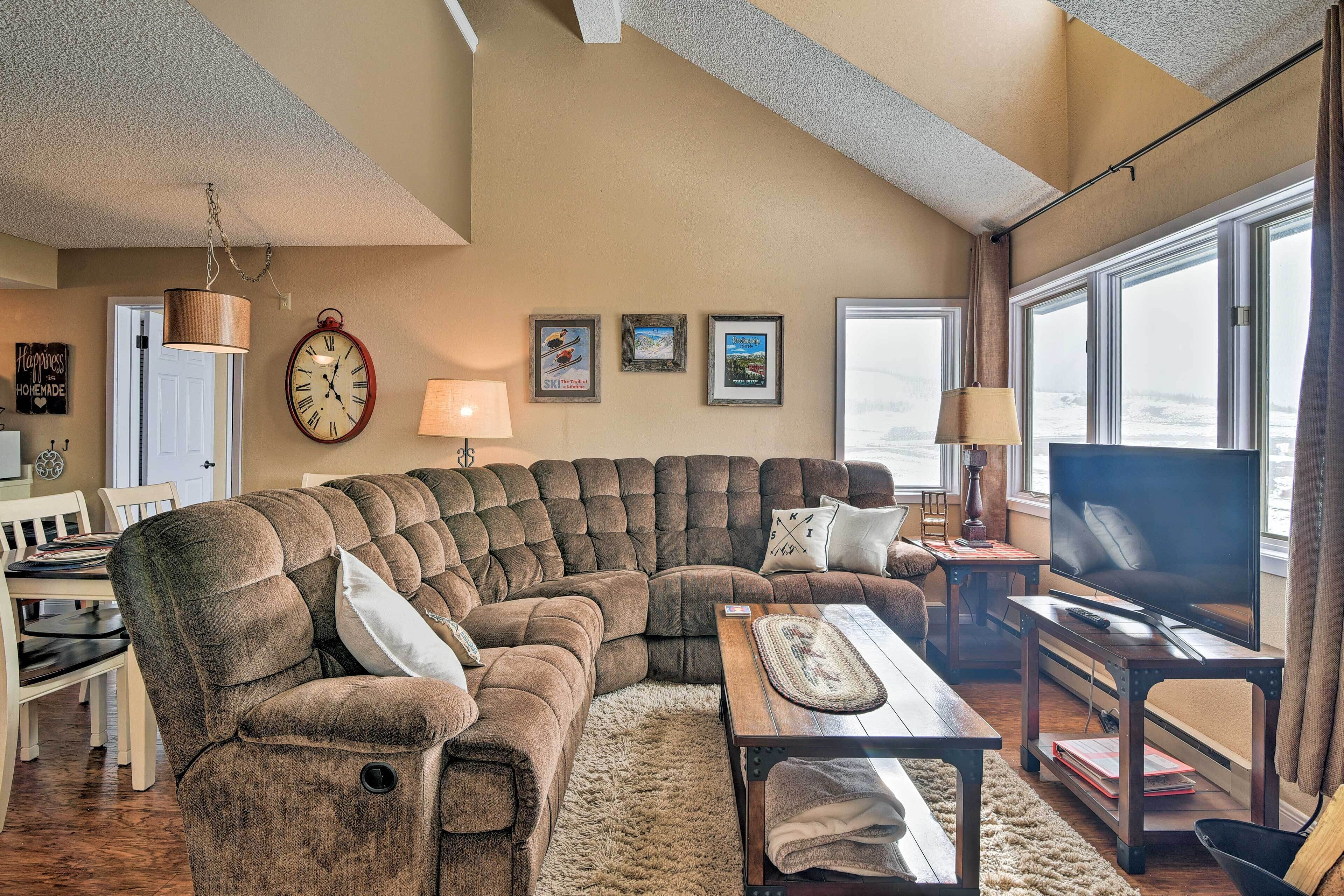 A living room with a sectional sofa, a flat-screen TV, a coffee table, and a dining area with a table and chairs.