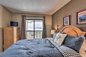 A bedroom with a large bed, a TV, a wooden wardrobe, and a balcony with a view. - Walk to Ski Lift: Mtn-view Granby Ranch Condo (Granby)