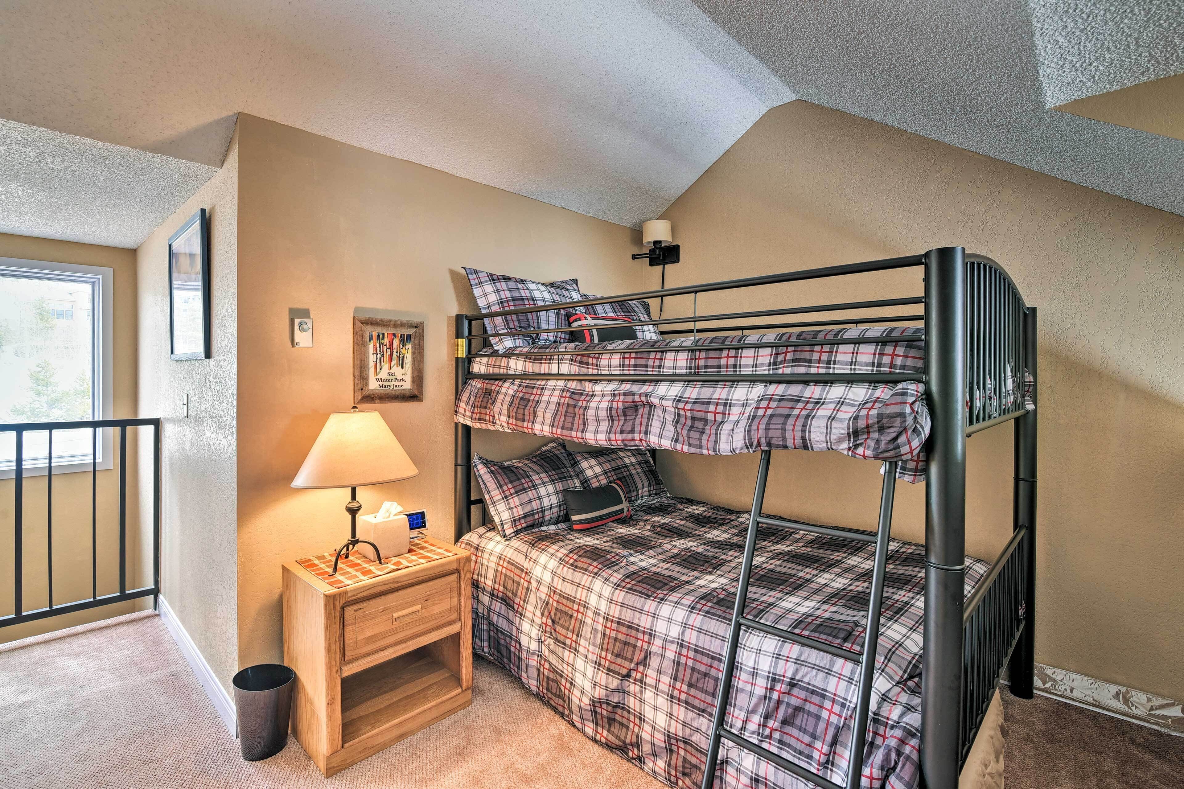 A bunk bed with plaid bedding, a bedside table with a lamp, and a small picture frame on the wall.