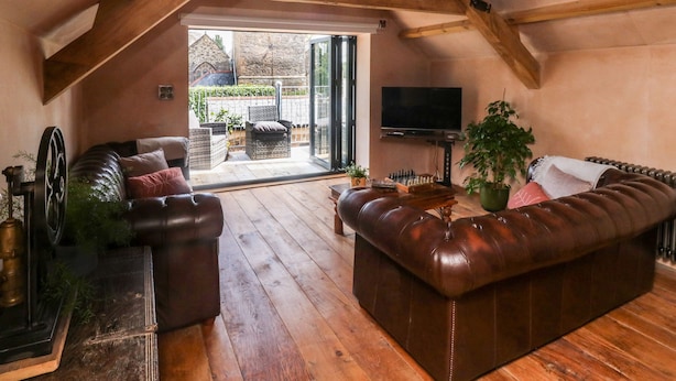 Un loft espacioso con techo de madera, un sofá de cuero, un televisor y vistas a un jardín a través de un ventanal corredero.