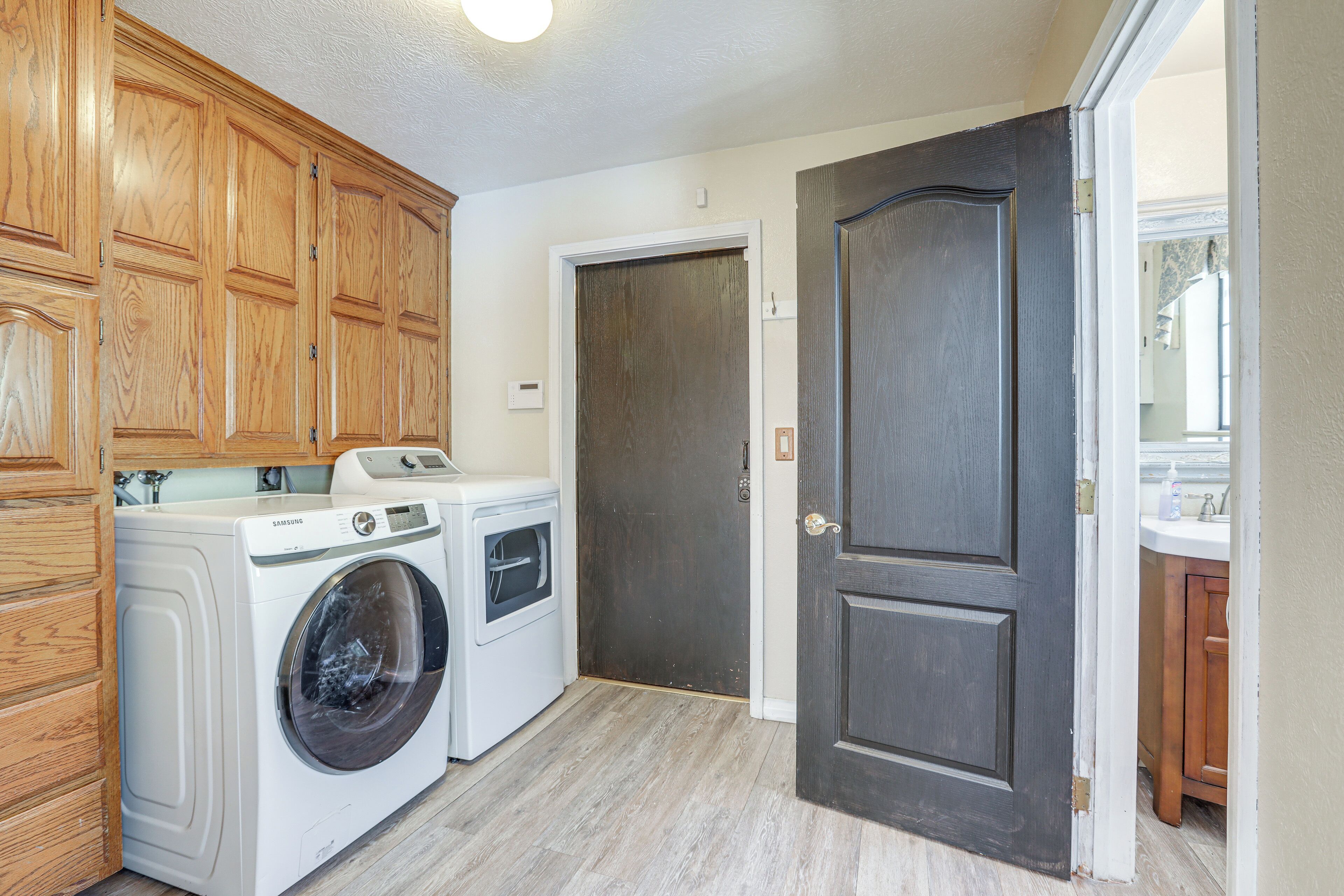 A laundry area with a washing machine and dryer, wooden cabinets, and a dark door.
