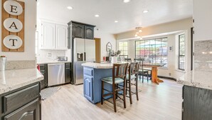 Una cocina moderna con armarios blancos, una isla azul y una zona de comedor con sillas de madera.
