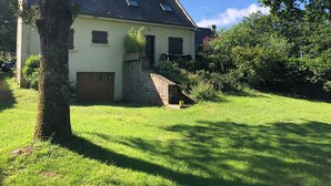 Une maison à deux étages, dotée d’un escalier en pierre menant à l’entrée, entourée d’une végétation luxuriante et d’une pelouse bien entretenue.
