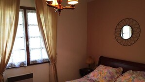 Une chambre à coucher avec un lit, des rideaux, un miroir fixé au mur et un luminaire au plafond.