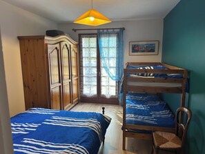 A bedroom with two bunk beds, a wooden wardrobe, a chair, a hanging light fixture, and a window with curtains. - Maison à Vannes (Séné)