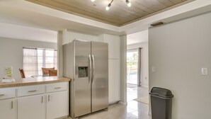 Une cuisine moderne avec des meubles blancs, un réfrigérateur en acier inoxydable et une poubelle.