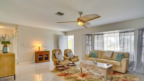 Un salon spacieux avec un canapé beige, deux fauteuils en cuir, une table basse et un ventilateur de plafond.