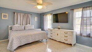Une chambre à coucher avec un lit, une commode, un ventilateur de plafond, une télévision et des rideaux.
