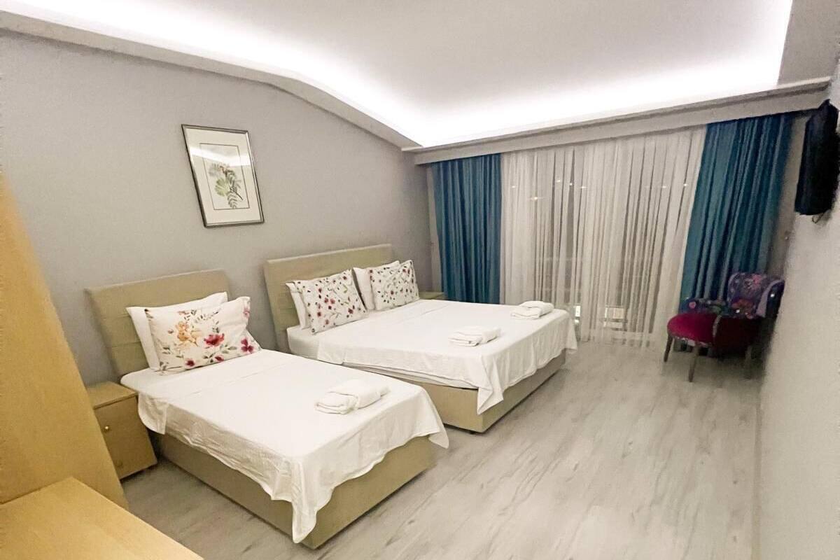 A hotel room with two beds, a small wooden table, a chair, and a window with curtains.