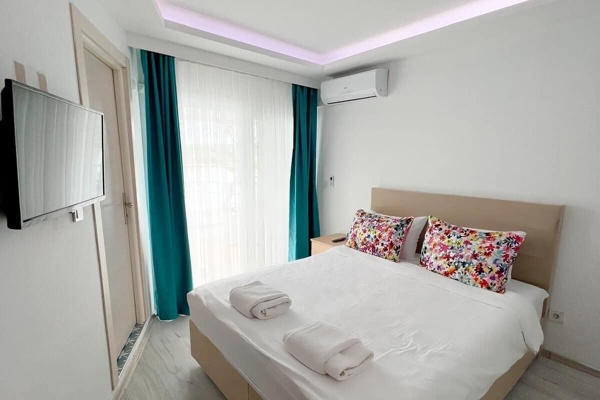 A hotel room with a bed, a TV, a window with curtains, and an air conditioning unit.