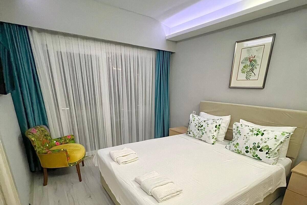 A neatly arranged hotel room with a bed, a chair, a bedside table, and a window with curtains.