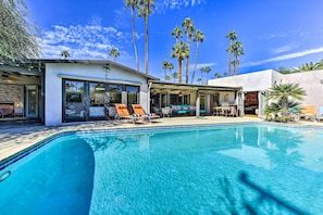 A modern pool area with clear blue water, lounge chairs, and a patio with a view of tall palm trees.