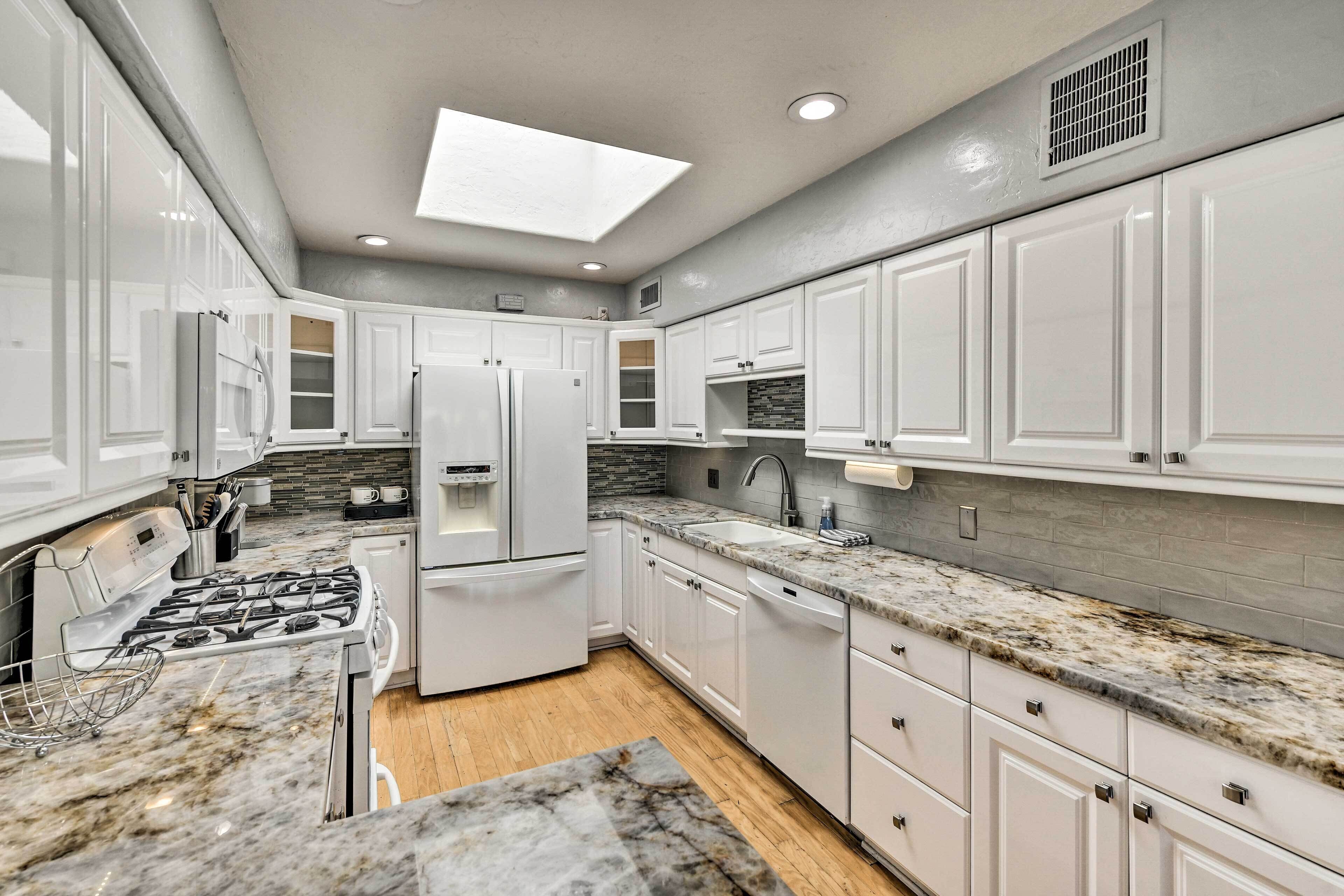 A modern kitchen with white cabinets, granite countertops, a gas stove, and a skylight.