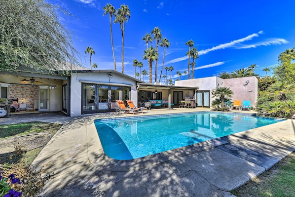 A modern house with a swimming pool, surrounded by palm trees and a clear blue sky.