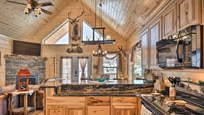 A rustic kitchen with wooden cabinets, a stone fireplace, and a large island with a sink. - Rio Grande National Forest Cabin: Views & Hot Tub (Del Norte)