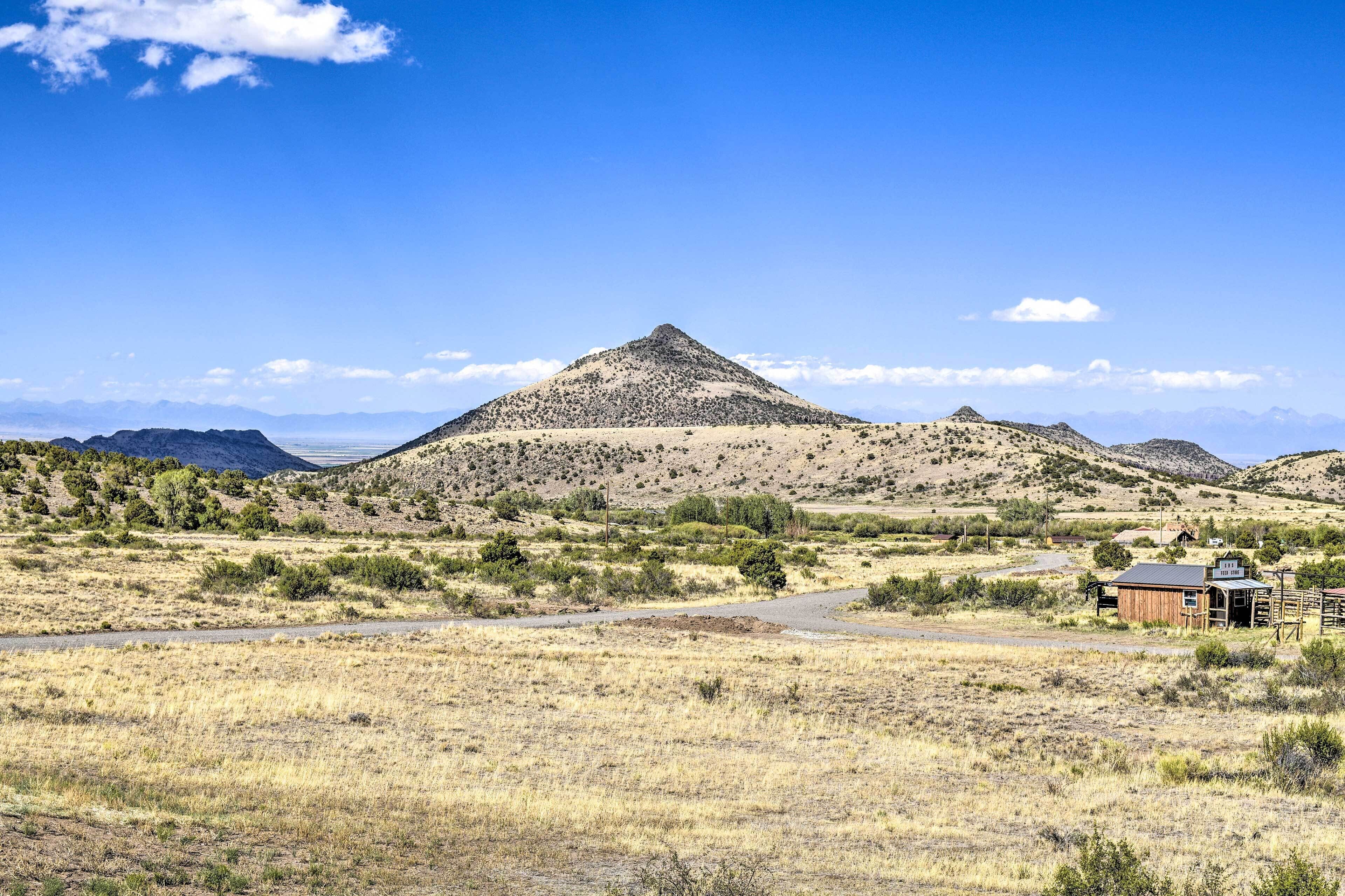 A rural landscape with a prominent hill, a dirt road, and a wooden cabin.