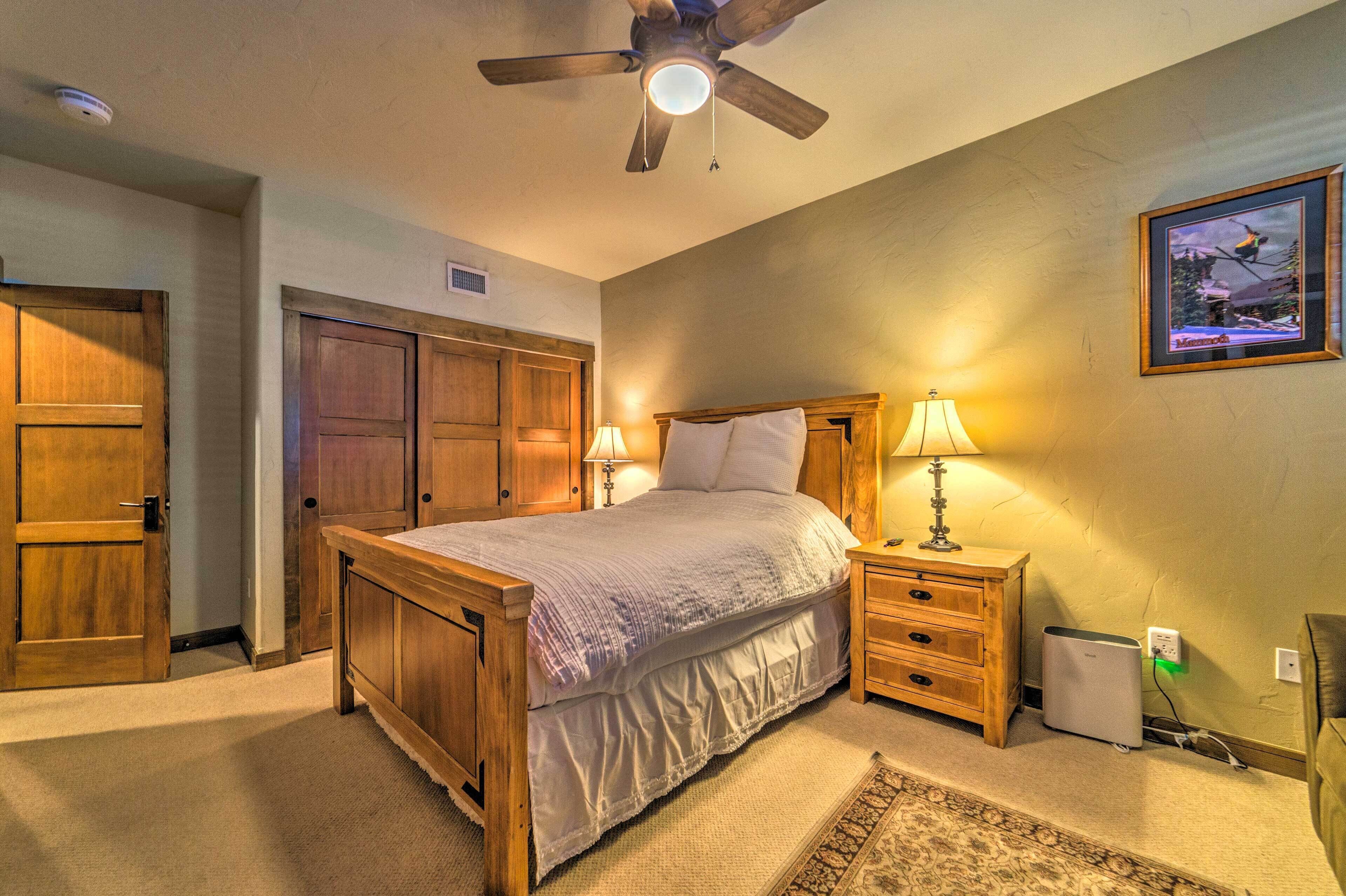 A bedroom with a wooden bed, two bedside tables, a ceiling fan, and a wall-mounted TV.