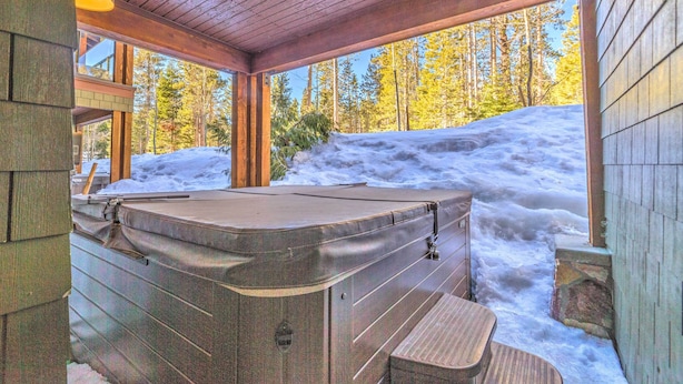 Une cabane en bois avec un jacuzzi et une vue sur une forêt enneigée.