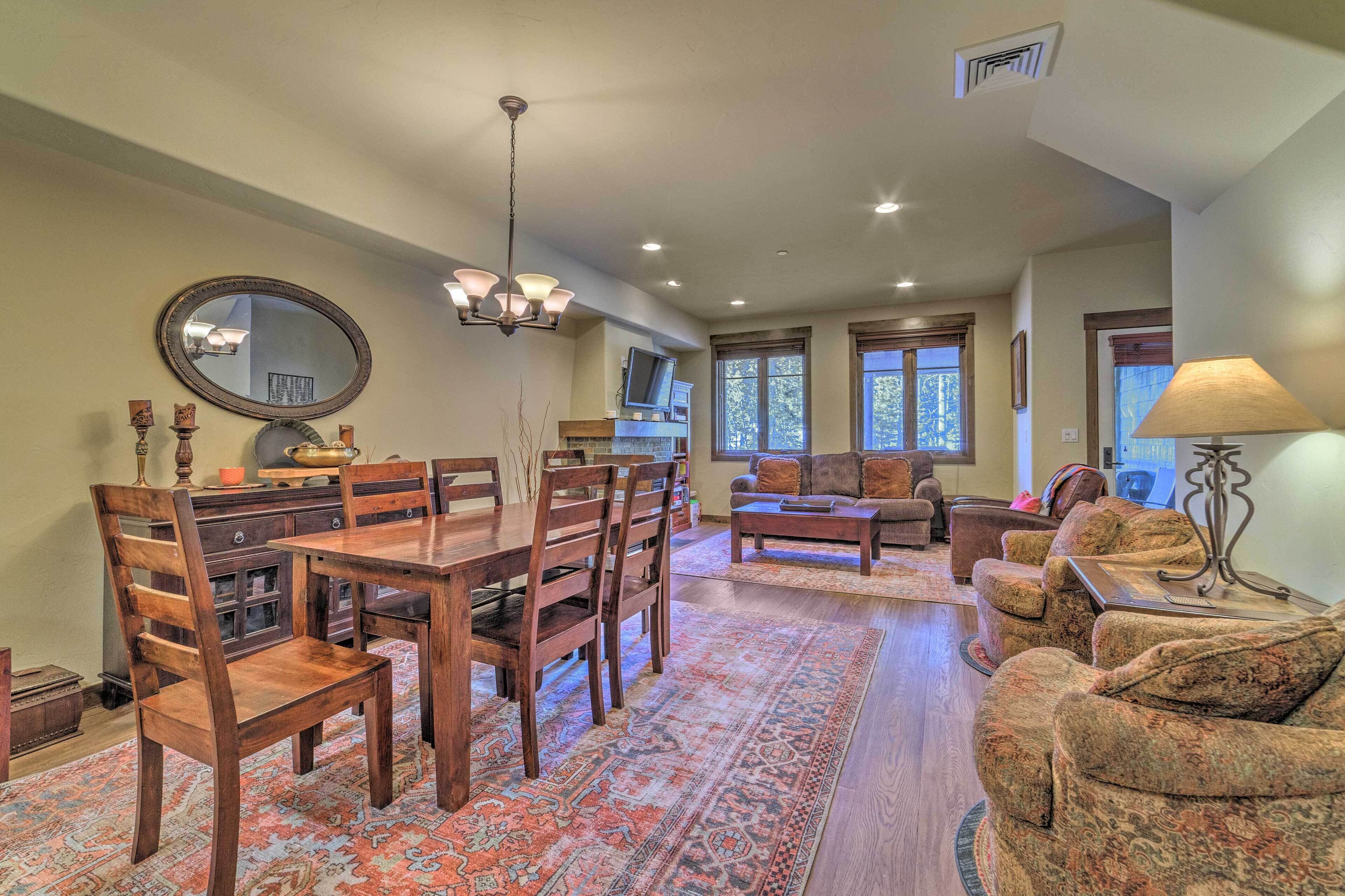 A spacious living room with a wooden dining table, chairs, a sofa, and a patterned rug.