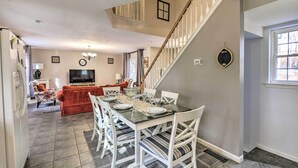 Ein Essbereich mit Glastisch und weißen Stühlen, eine Treppe sowie ein Wohnzimmer mit rotem Sofa und Fernseher.