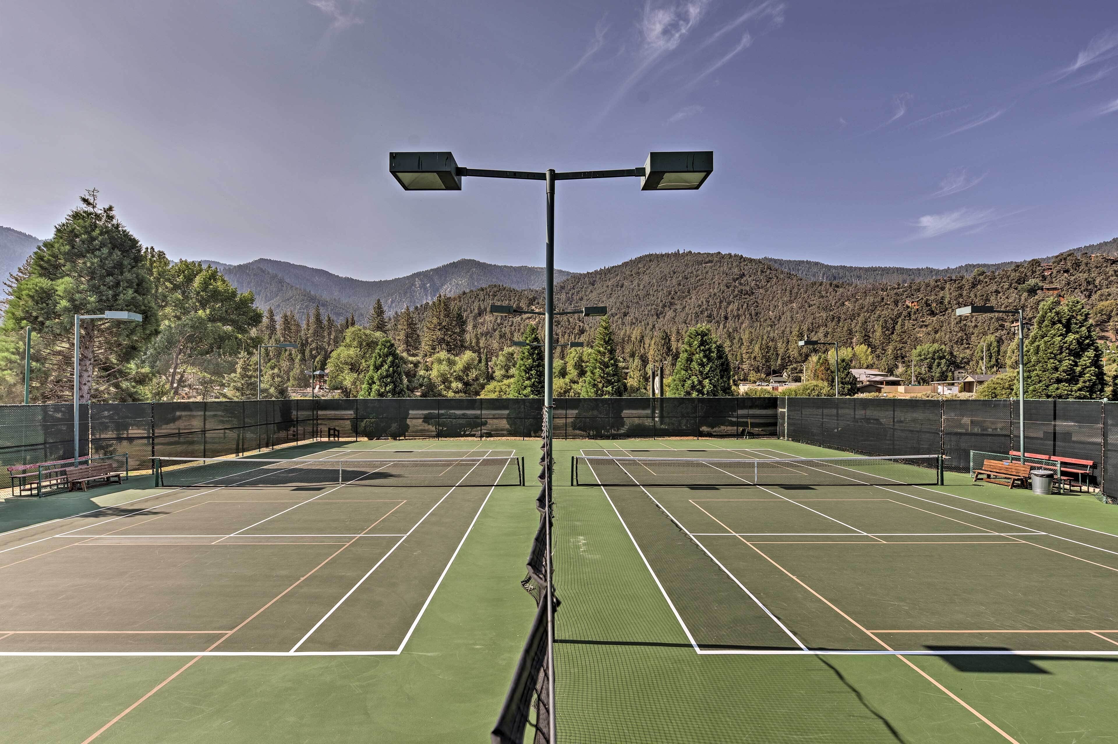 A tennis court with a net, benches, and street lamps.
