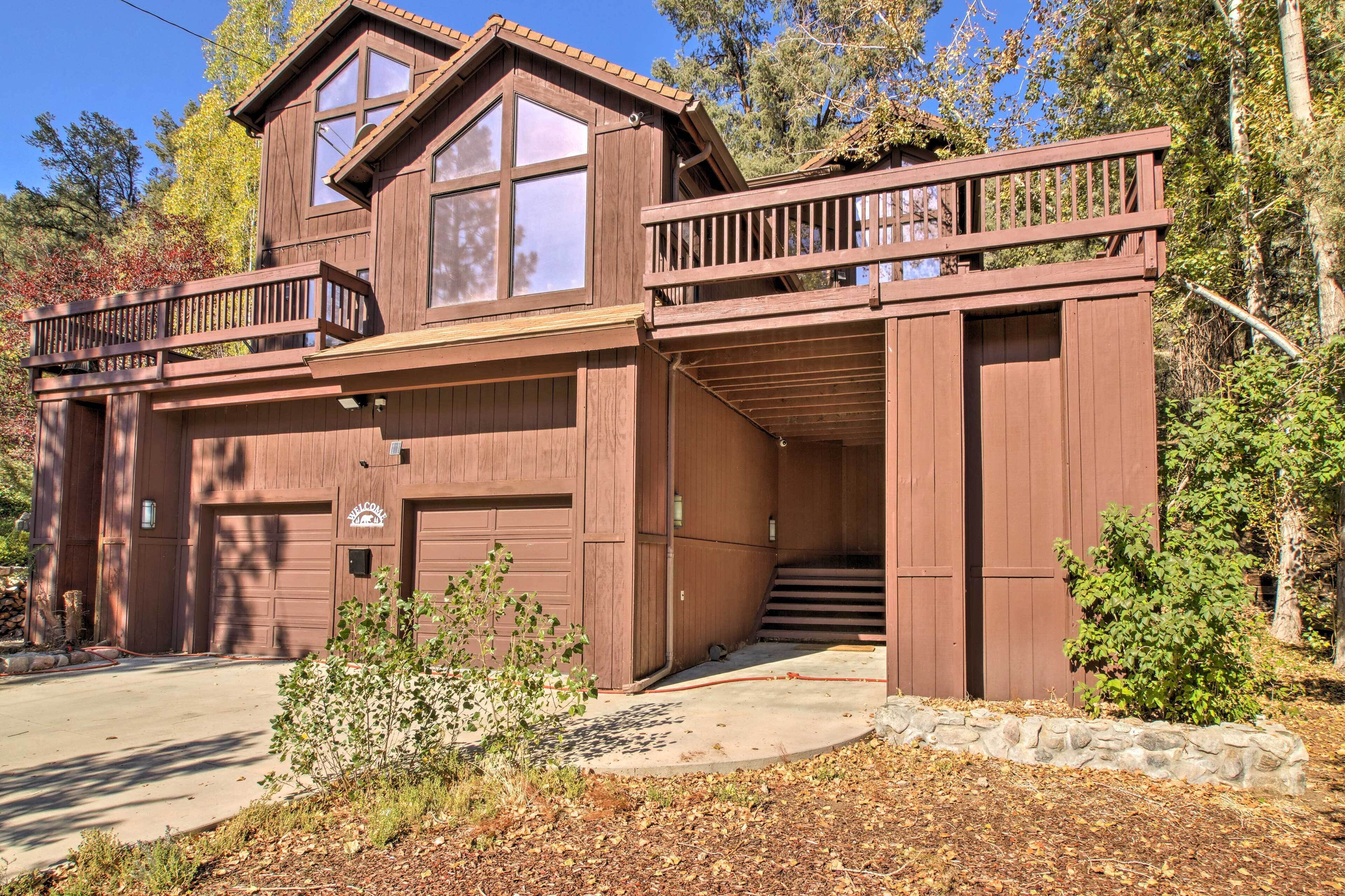 A two-story wooden cabin with a garage, a balcony, and a stone retaining wall.