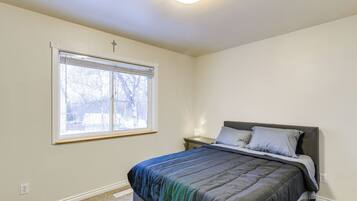 A bedroom with a bed, a nightstand, a window with blinds, and a cross on the wall.