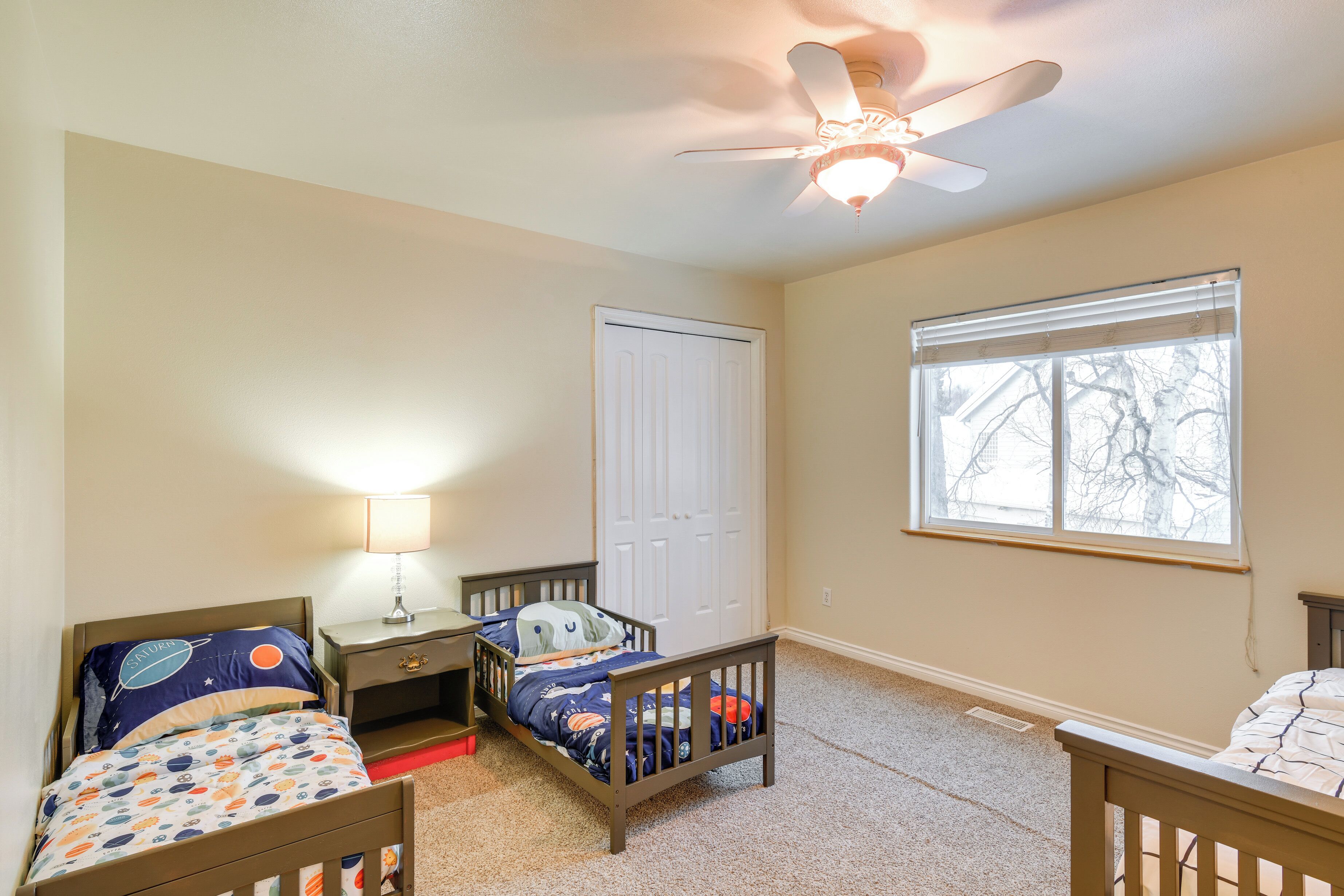 A bedroom with two beds, a ceiling fan, a window, and a door.
