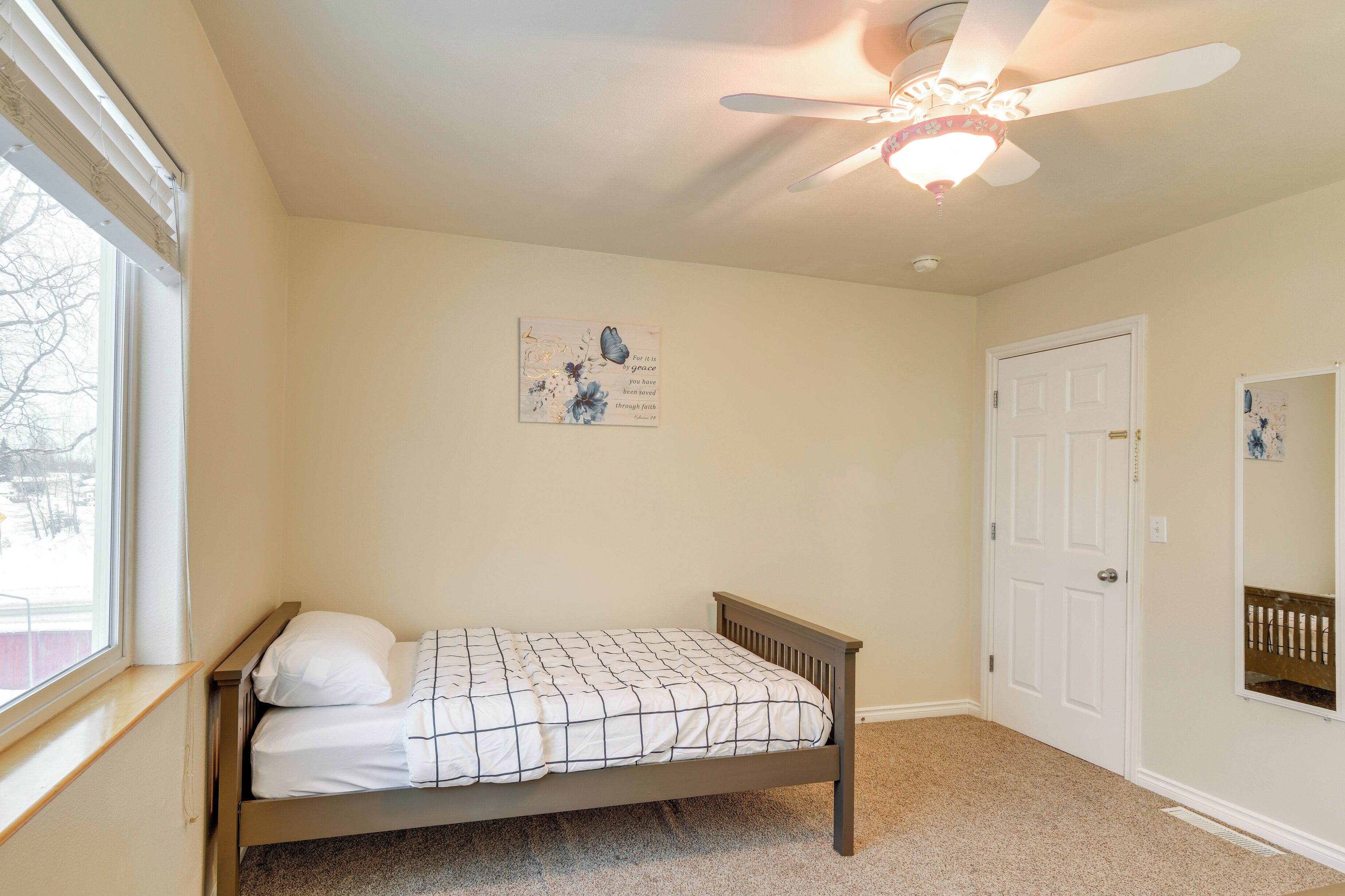A bedroom with a single bed, a ceiling fan, a window, and a door.