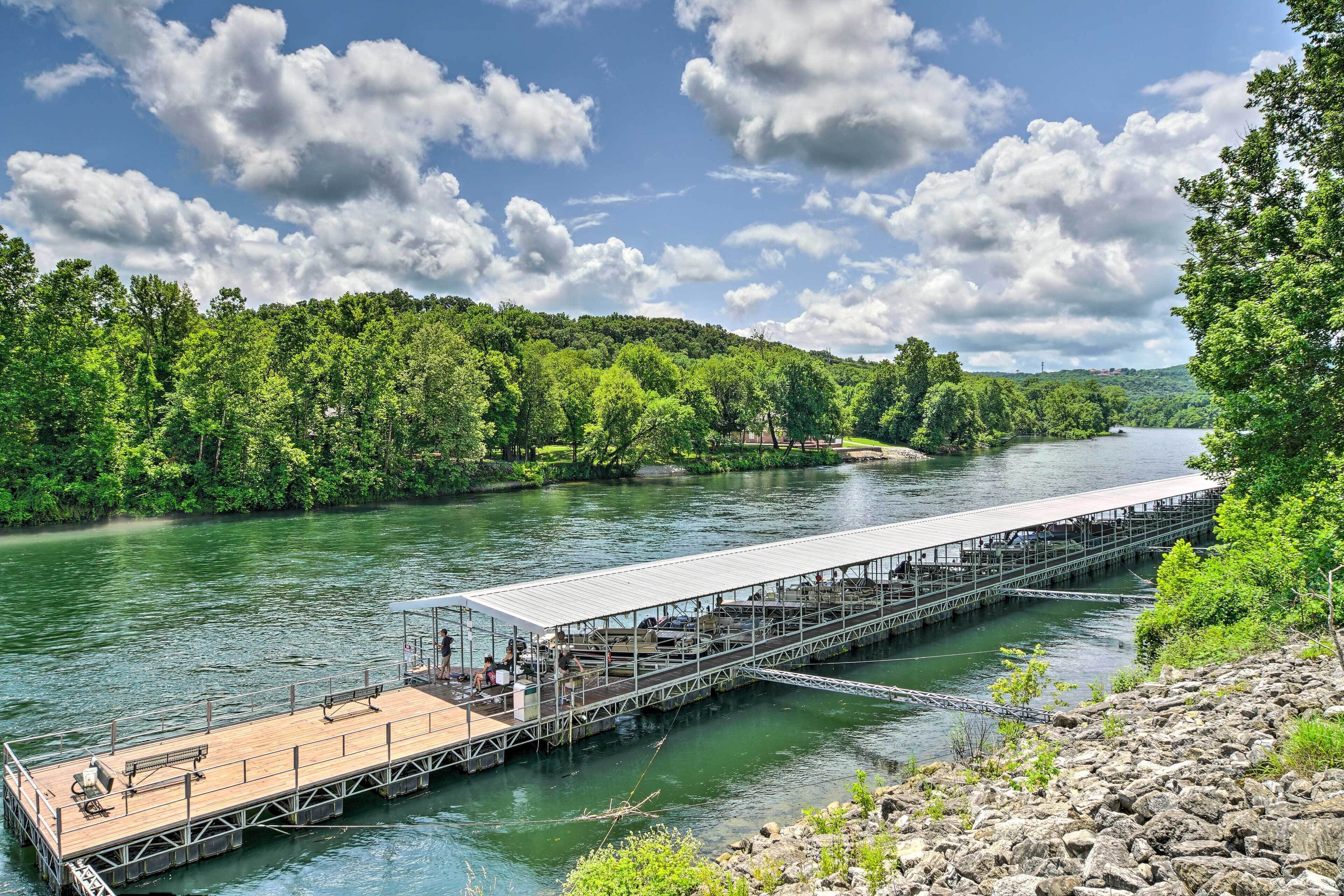 A wooden pier extending into a river, surrounded by lush greenery and a clear sky.