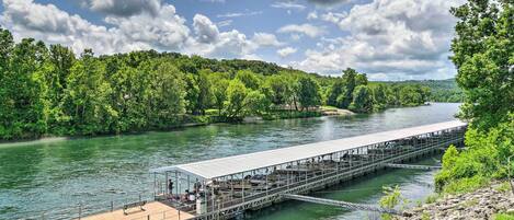 A wooden pier extending into a river, surrounded by lush greenery and a clear sky.