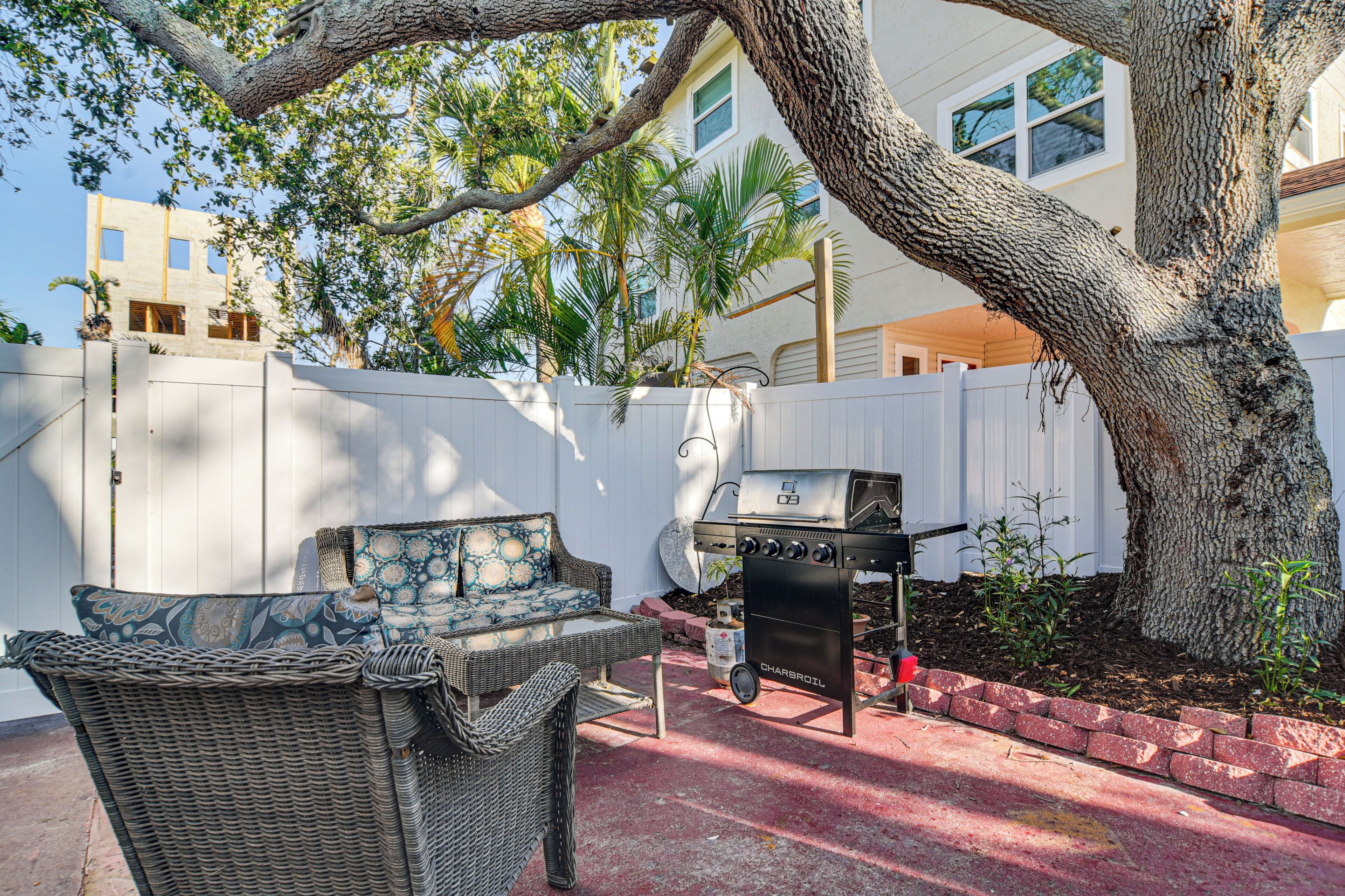 Un patio con mobili in vimini, un barbecue e un albero grande.