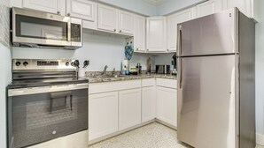 A kitchen with white cabinets, stainless steel appliances including a microwave, oven, and refrigerator, and a speckled floor. - Indian Rocks Beach Retreat, Walk to Gulf & Beaches (Indian Rocks Beach)