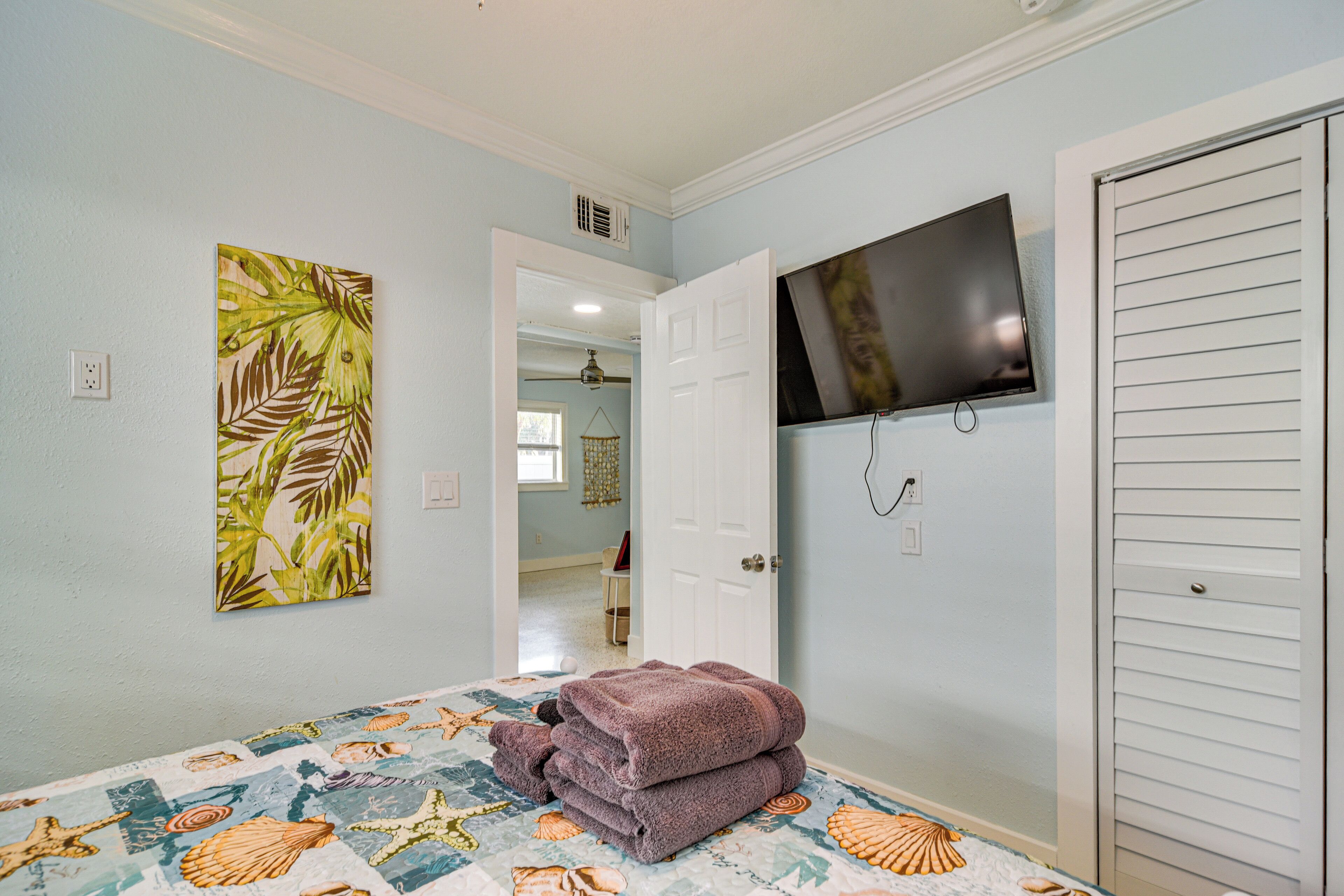 Un dormitorio con cama, televisor, puerta y un cuadro en la pared.