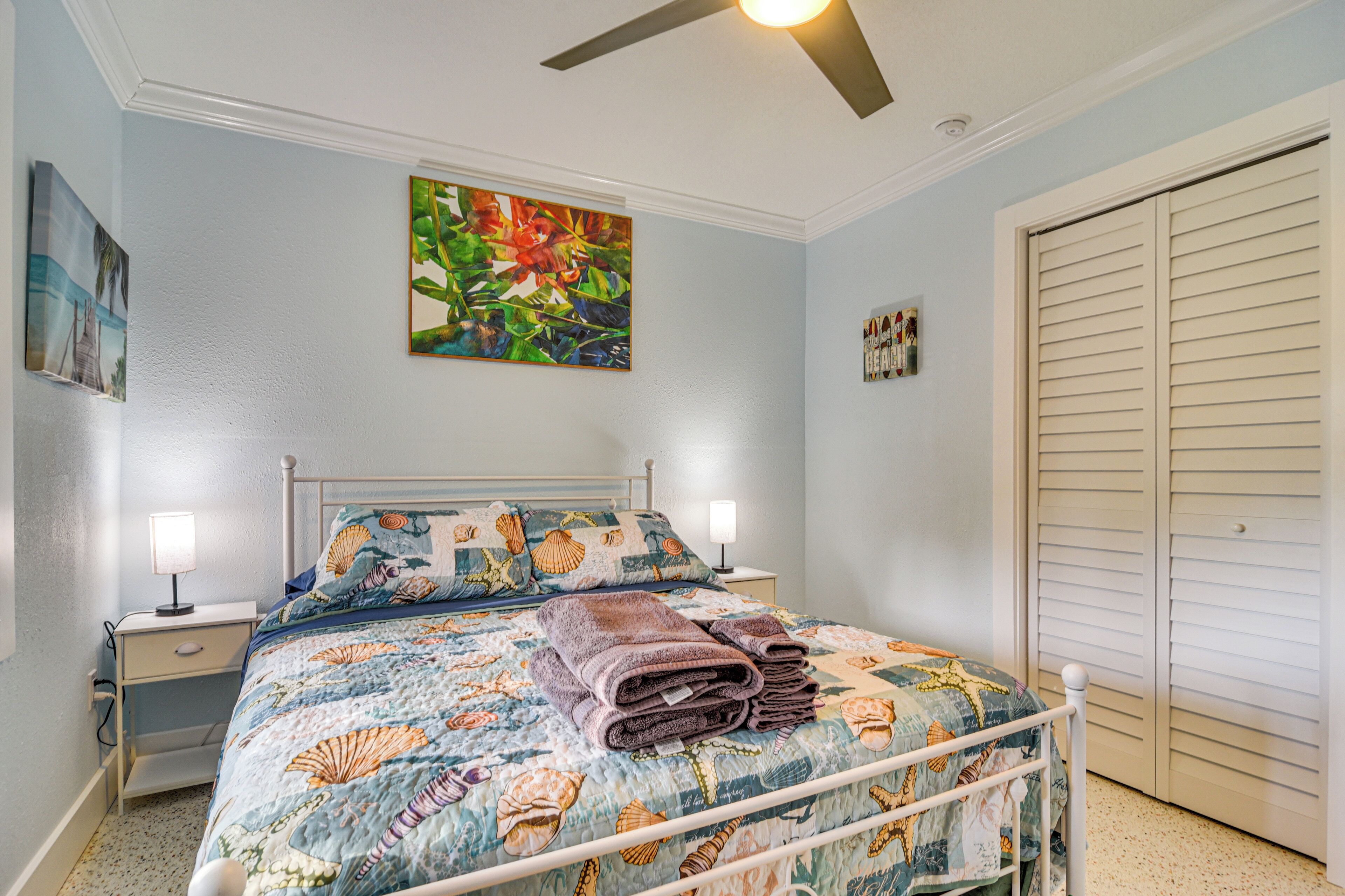 A bedroom with a bed, two bedside tables, a ceiling fan, and a door.