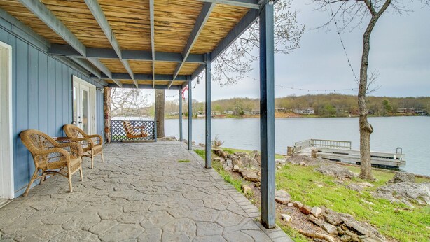Un patio techado con piso de piedra, sillas de mimbre y vista a un lago.