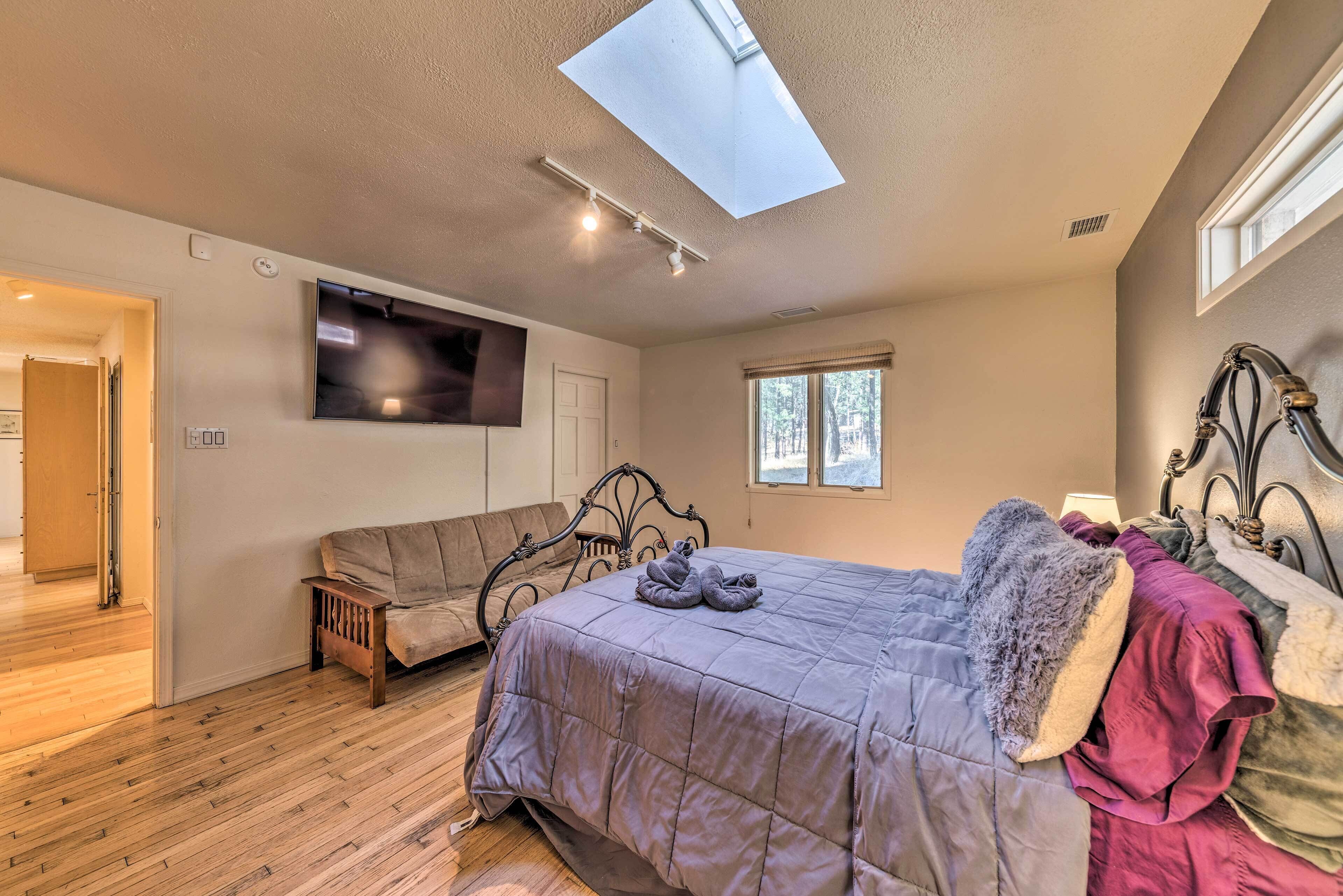 A bedroom with a bed, a bench, a TV, a skylight, and a window.