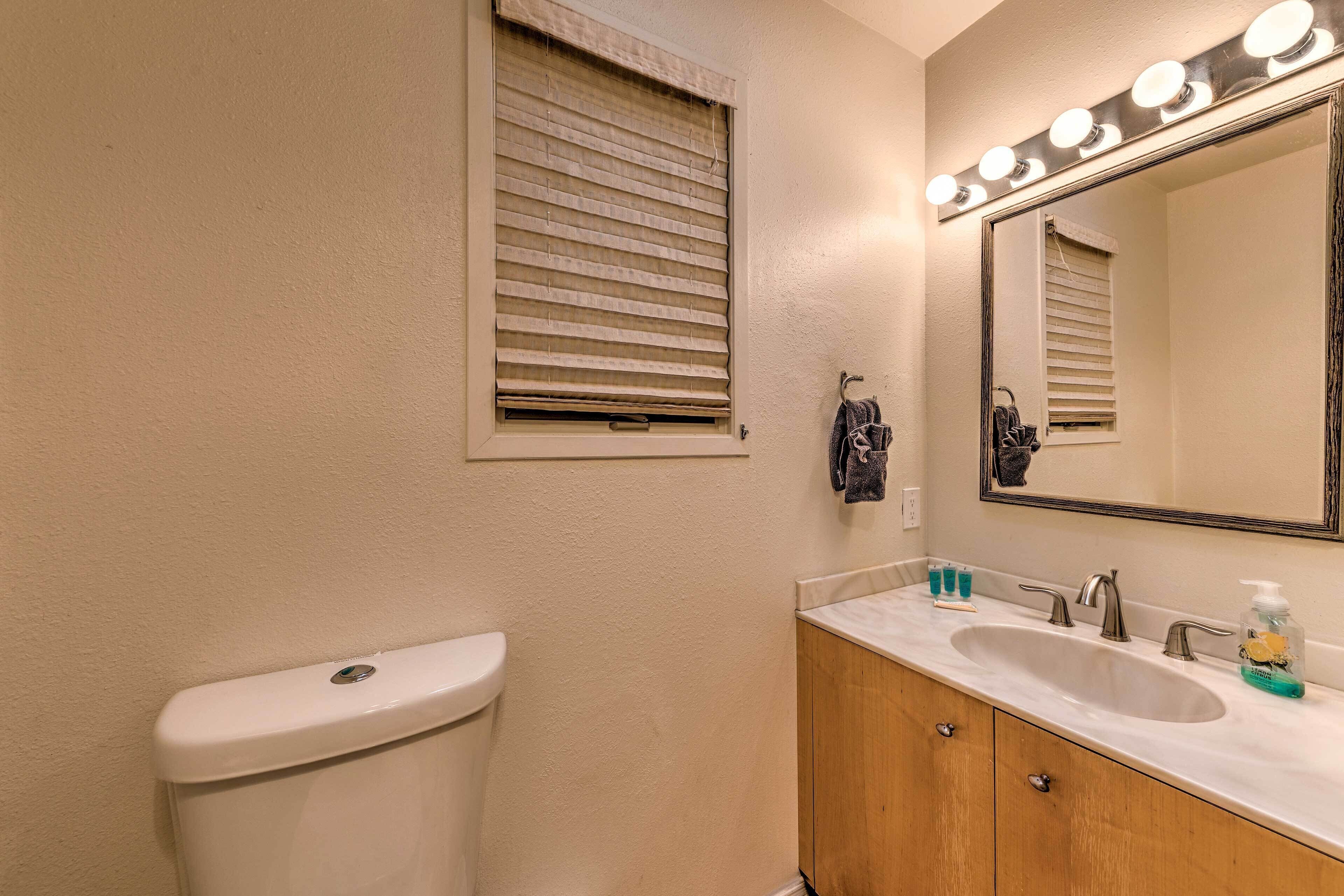 Un baño con inodoro, lavabo, tocador, espejo y ventana con persianas.